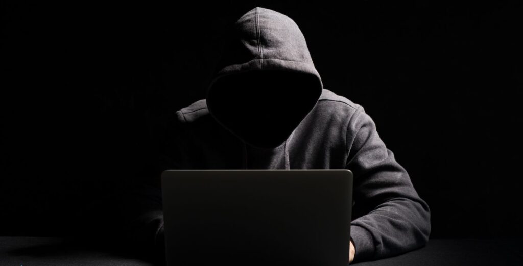 Hacker in dark hoodie using laptop – warning image for AI tool scams and dark patterns
