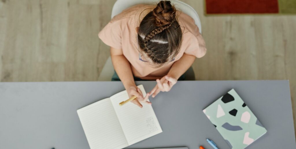 Young neurodivergent student using AI tools and a planner at a desk, representing focus and accessibility in learning